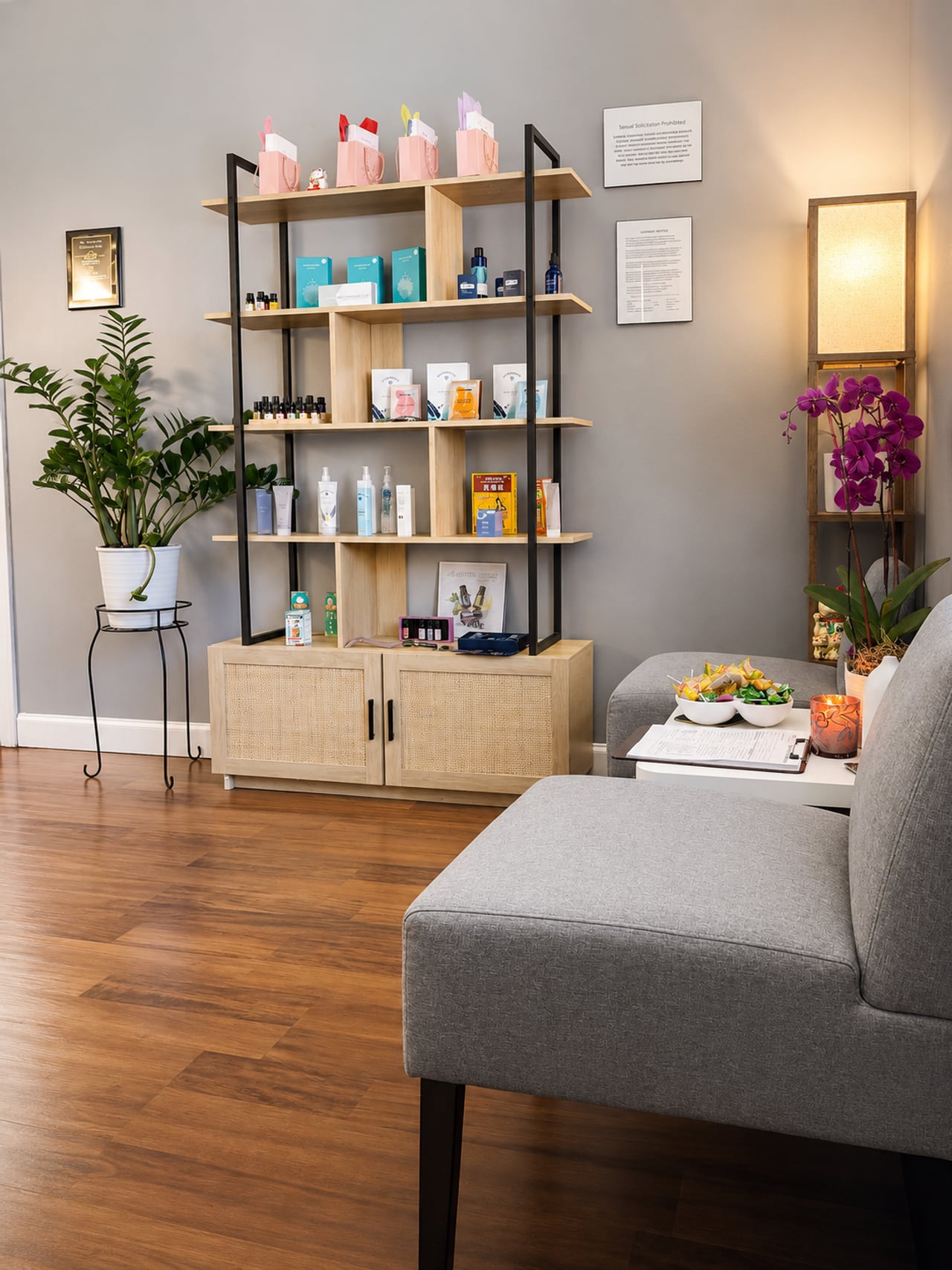 The calm reception lounge at TAO Therapeutic Massage Spa in Vienna, VA — a wood shelf of curated skincare, a fresh purple orchid, a leafy plant and a soft linen sofa