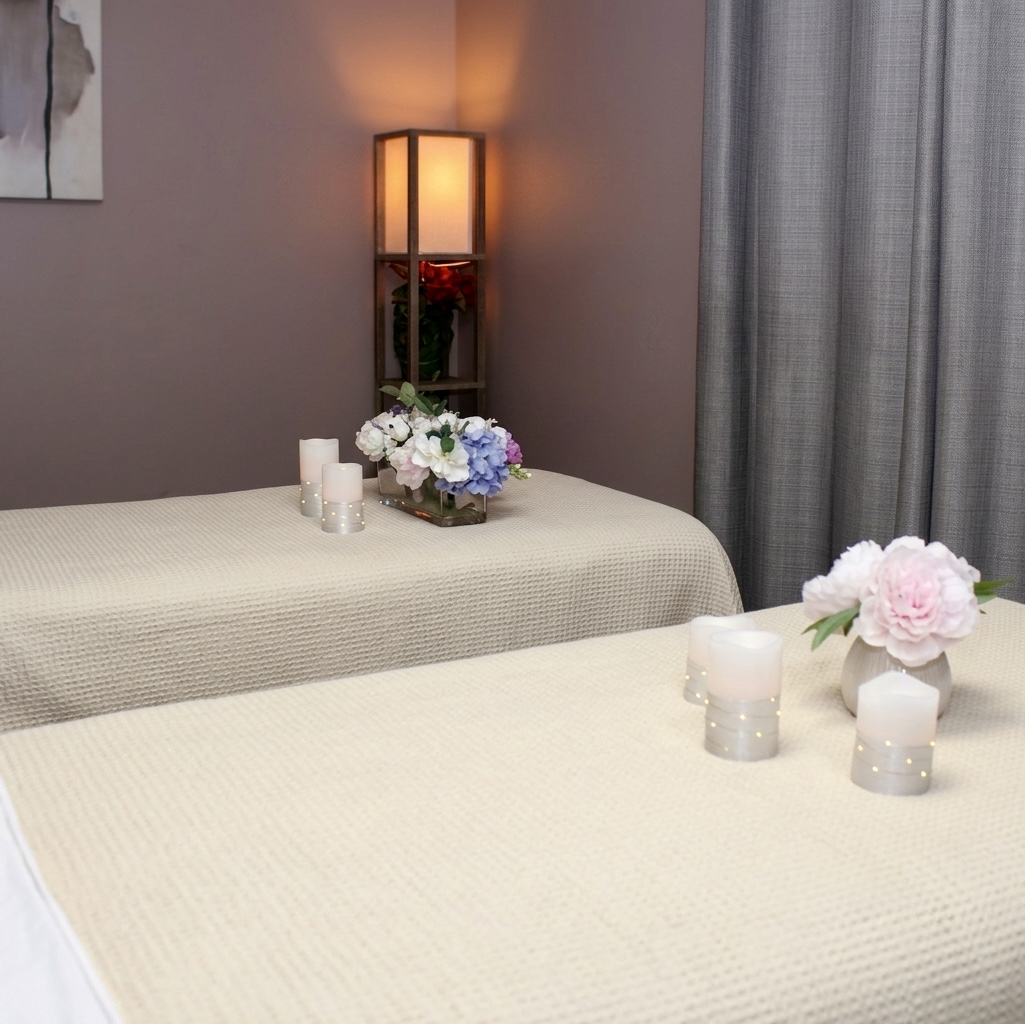 The couples treatment room at TAO Therapeutic Massage Spa — two side-by-side tables draped in ivory linen with candles and fresh flowers